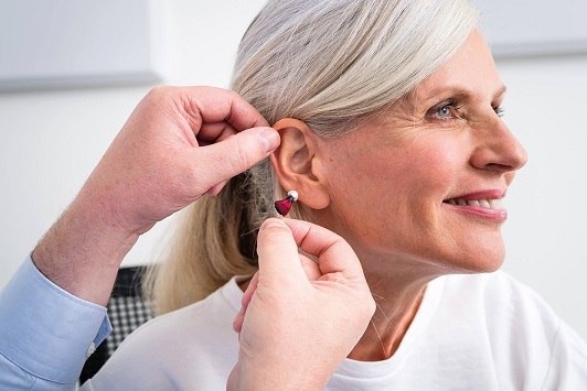 Ältere Frau bekommt ein modernes Hörgerät eingesetzt, Hörhilfe für Senioren.